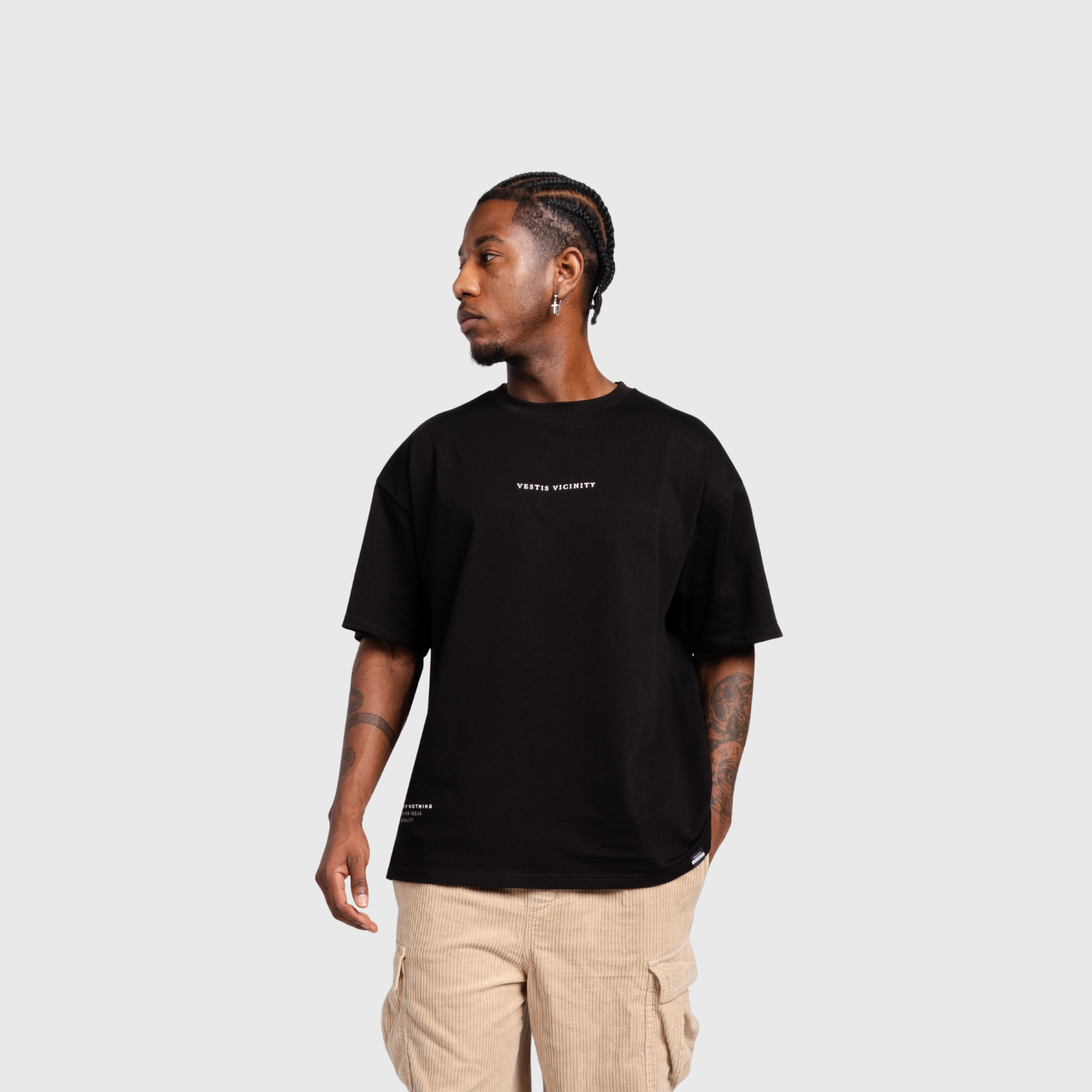 Model wearing a black oversized T-shirt and beige cargo pants, facing slightly to the side. The shirt features a small white text design on the chest.