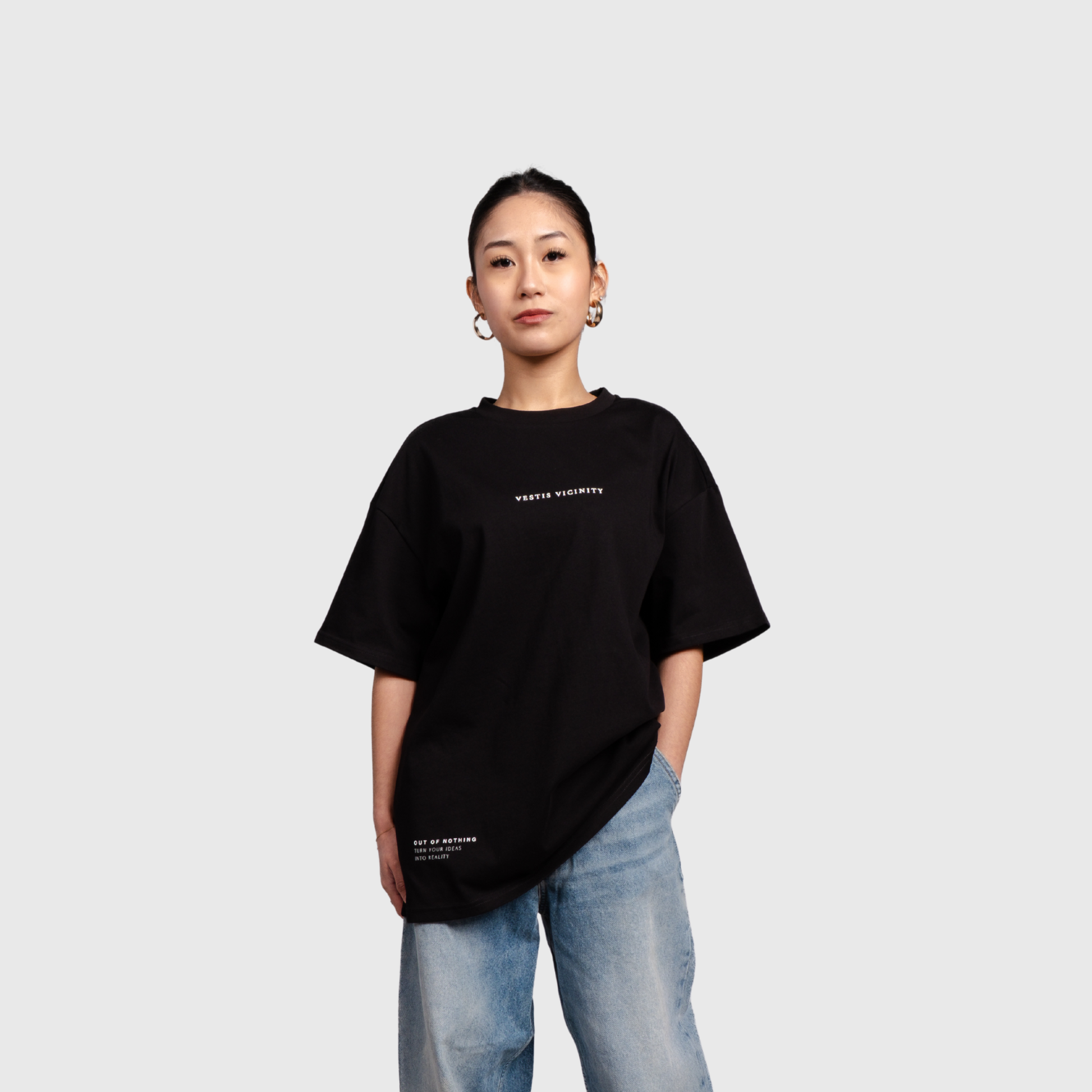 Model wearing a black oversized graphic T-shirt and light blue jeans, facing forward. The shirt features a small white text design on the chest