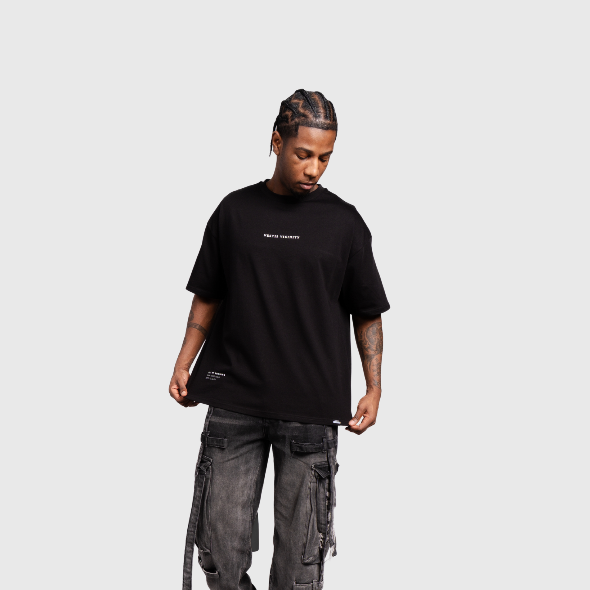 Model wearing a black oversized graphic T-shirt and dark cargo pants, facing forward. The shirt features a small white text design on the chest