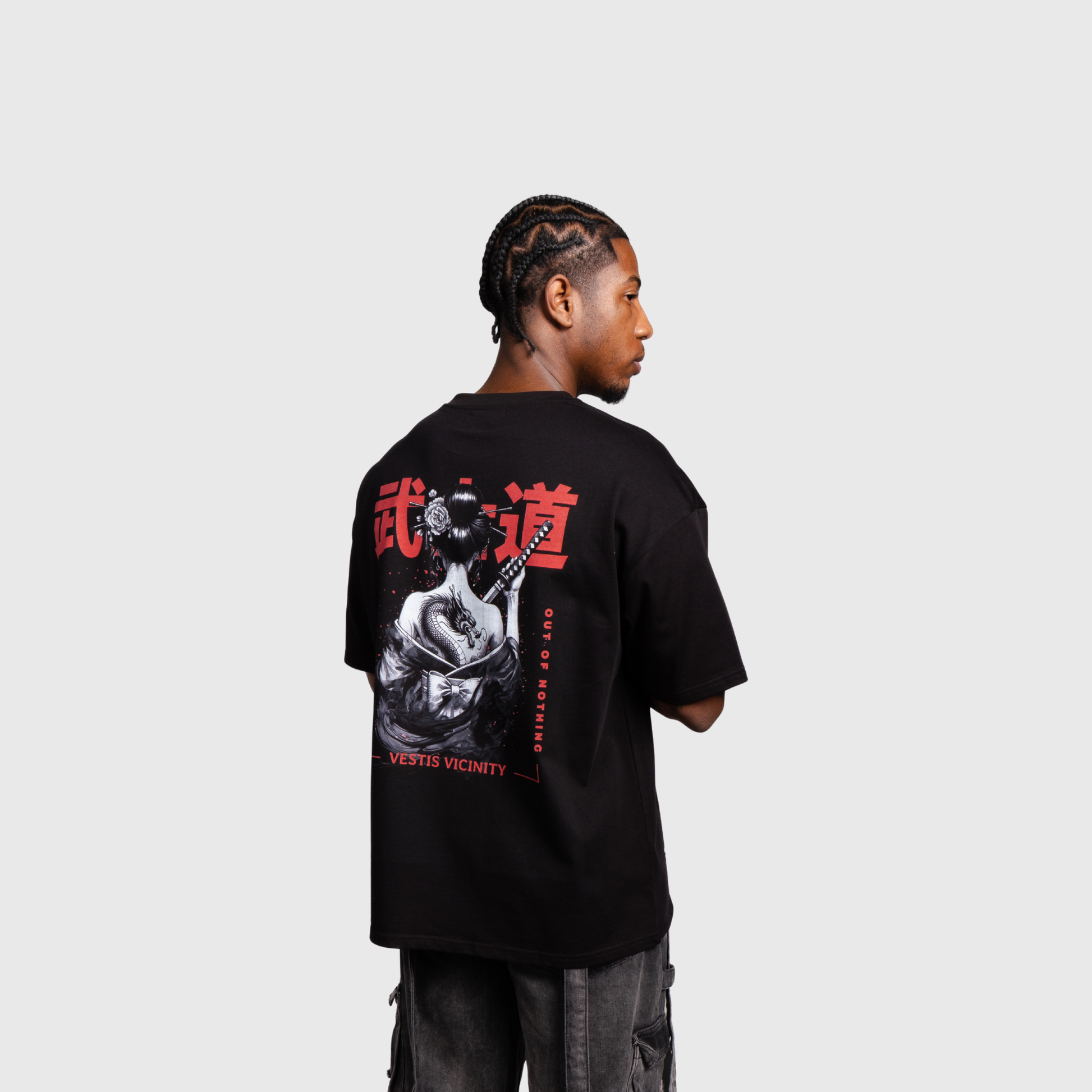 Model turned slightly away from the camera wearing a black oversized T-shirt. The back graphic shows a warrior illustration with red Japanese-style typography and red design accents.