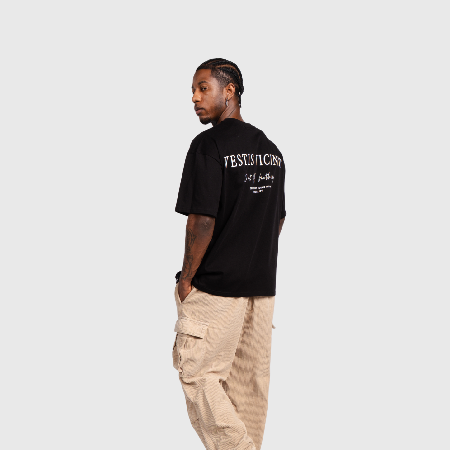 Side view of a model wearing a black oversized T-shirt and beige cargo pants. The back typography graphic is partially visible from the side angle